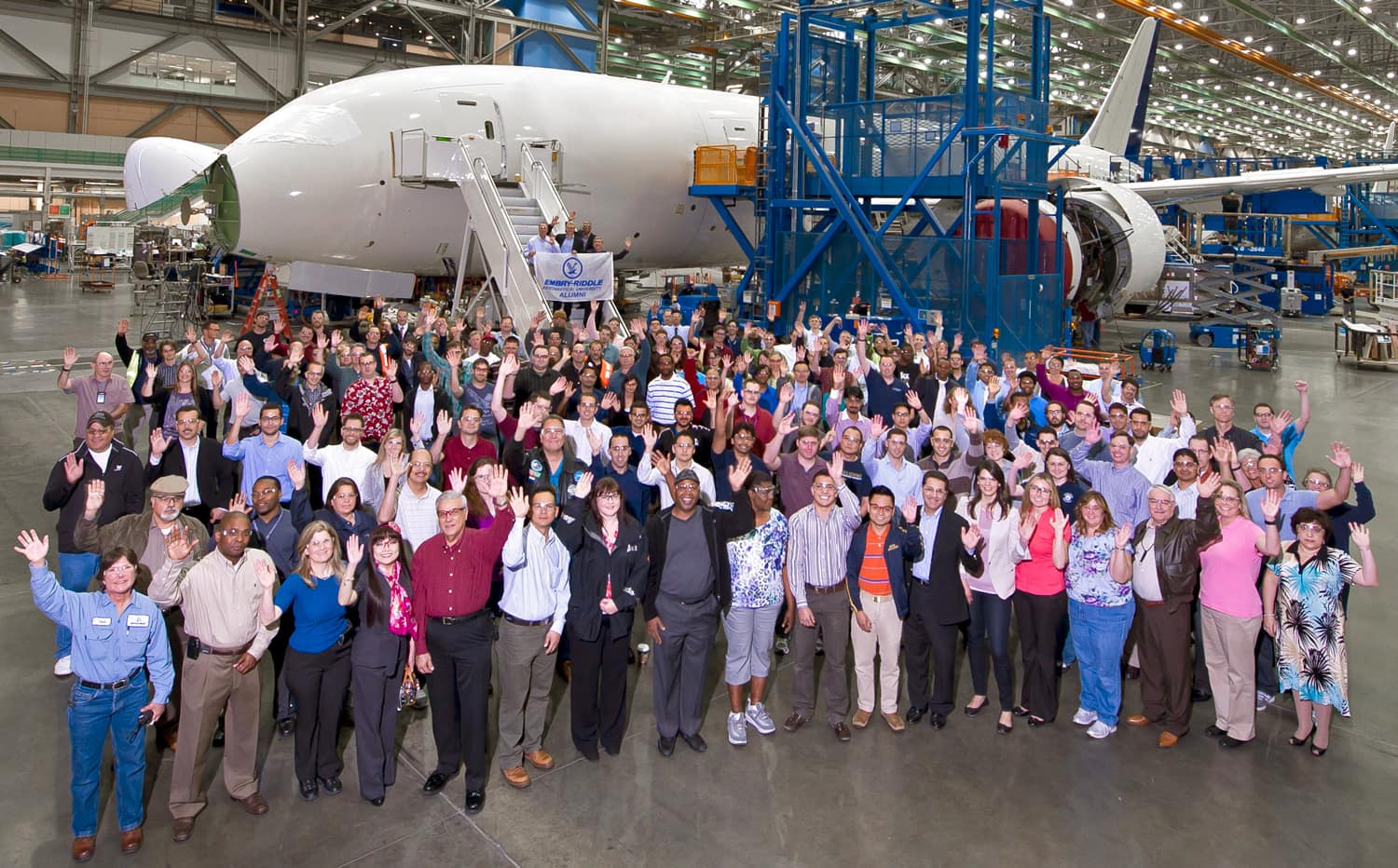 Group of ERAU alumni at a Boeing facility, in front of a large jet plane being built.