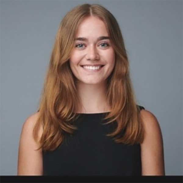 Gretchen, with long red hair and wearing a sleeveless top, smiles confidently.