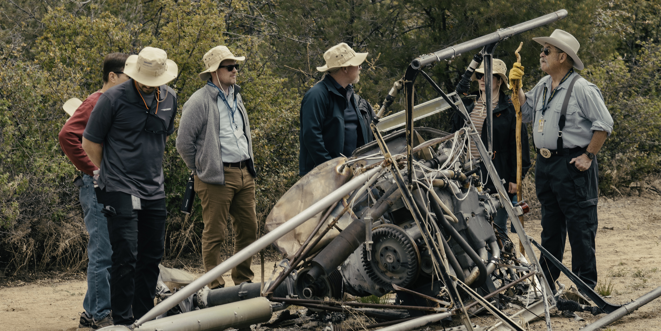 Group of people surround crashed helicopter in a field.