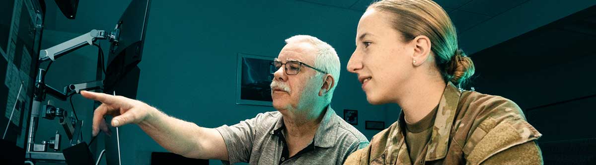 Faculty points at computer screen while female cadet looks on