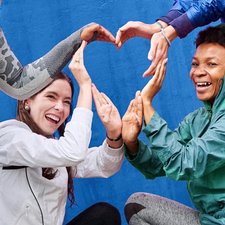 Four smiling students use their hands to shape one large heart.