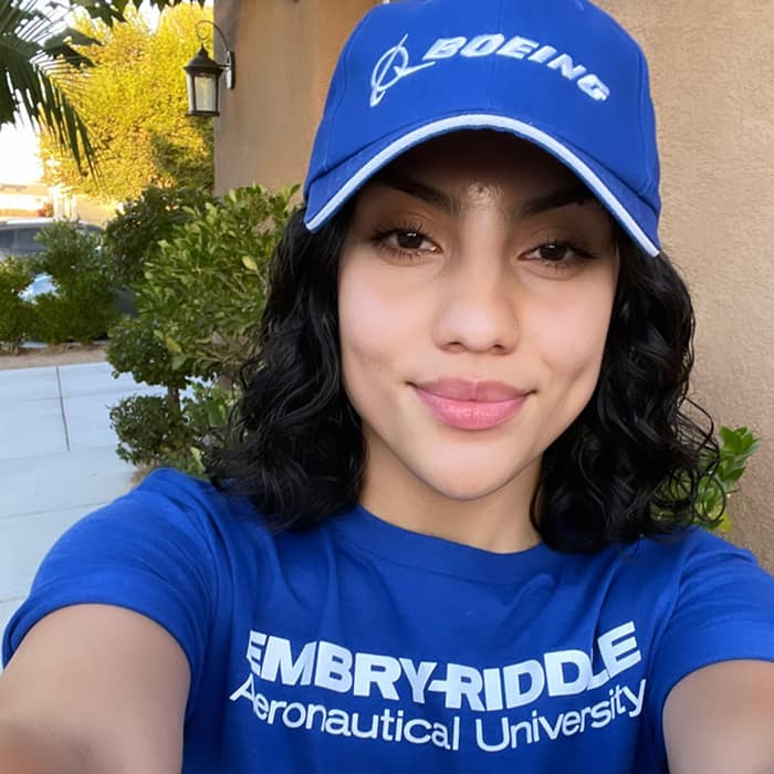 Woman with an olive complexion smiles for a selfie. She's wearing a Boeing cap and Embry-Riddle t-shirt.