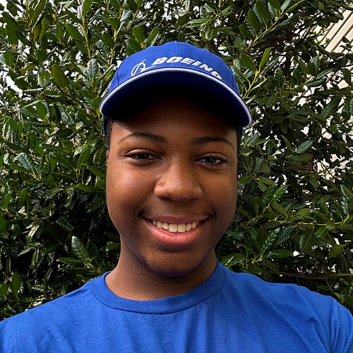 Black man in a Boeing cap smiles in front of a tree.