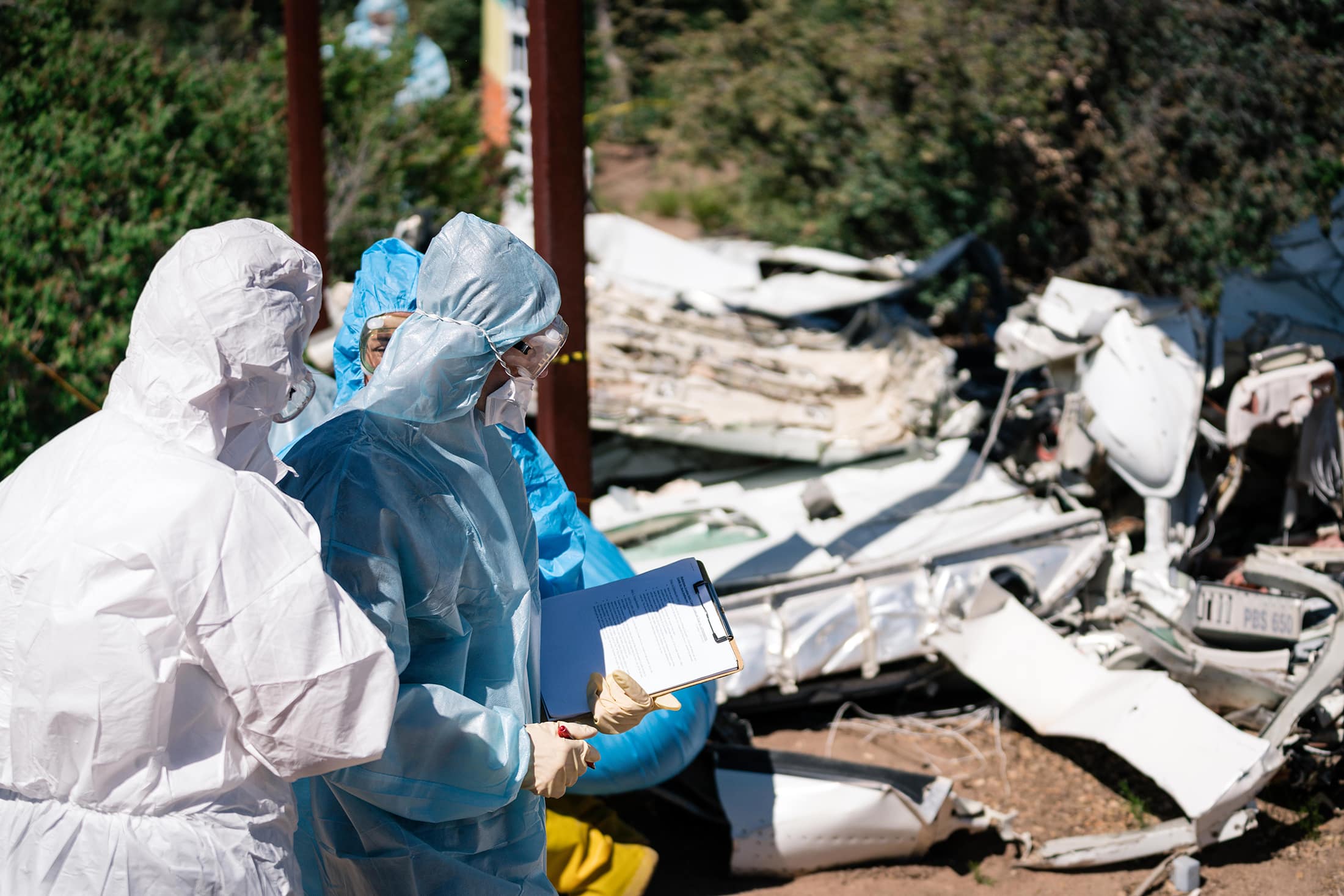People wearing protective suits looking at a plane crash.