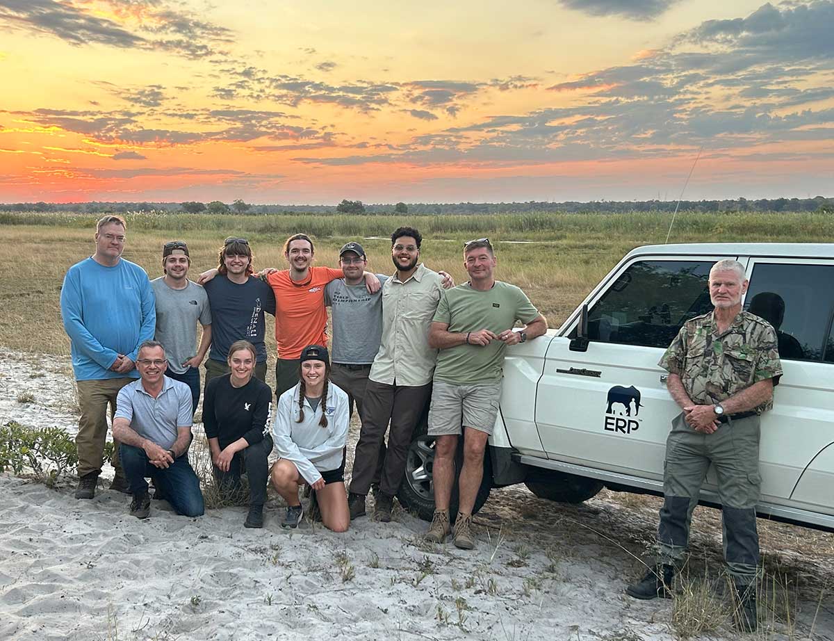 Team poses with truck on African Plain with colorful sunset