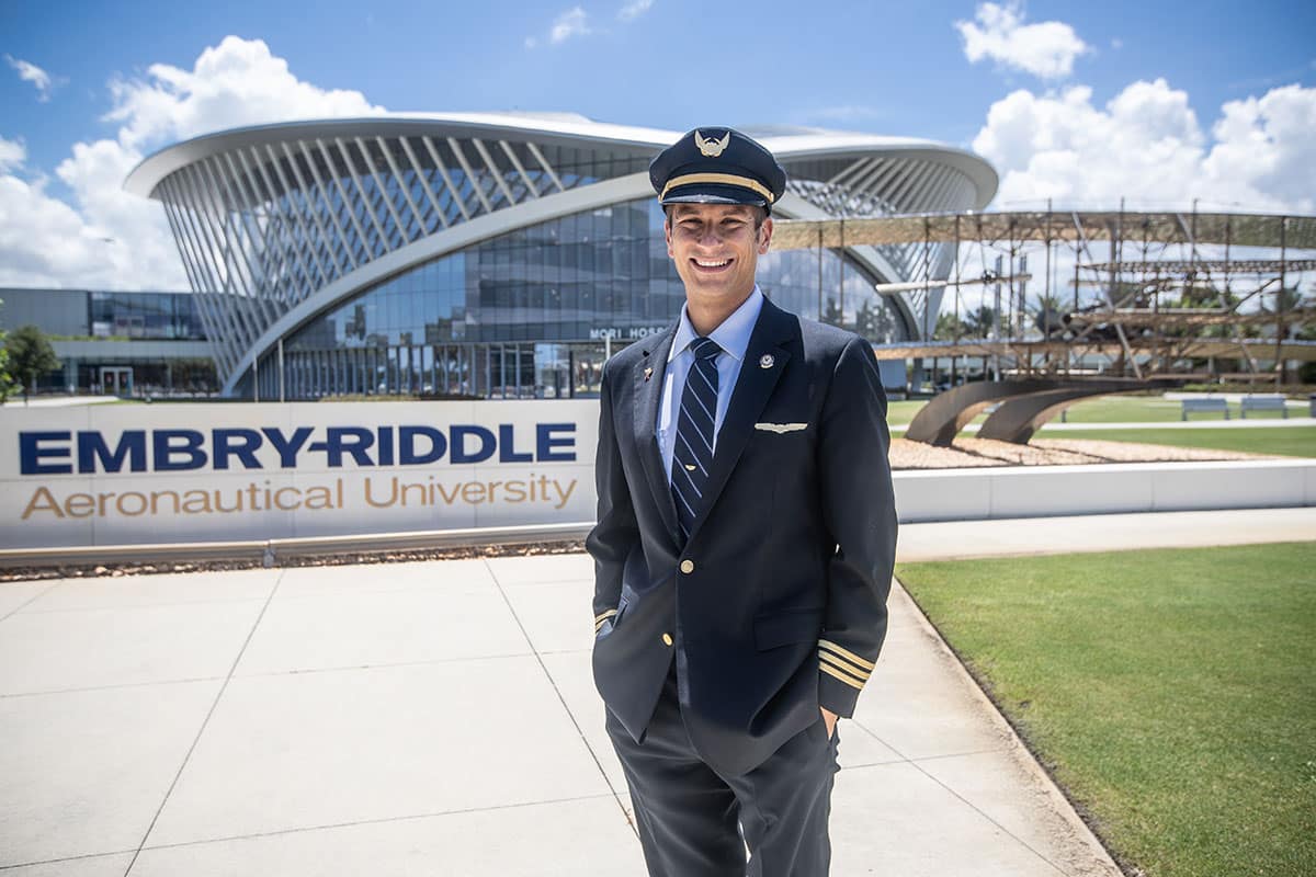 Costas Syvillis in his pilot's uniform stadning in front of the Embry-Riddle Aeronautical University sign