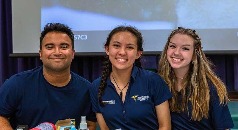 Three students sitting at table smile