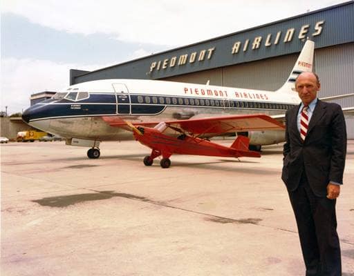 Tom Davis in a suit with Piedmond Airlines jet and Piper Cub in the background