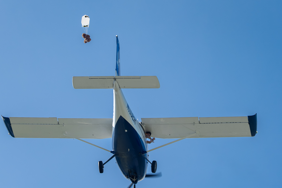 Airplane against blue sky with teddy bear descending from a small parachute